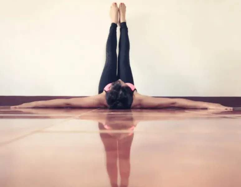 A woman lying on the ground with her legs resting on the wall and her arms spread out to the sides.