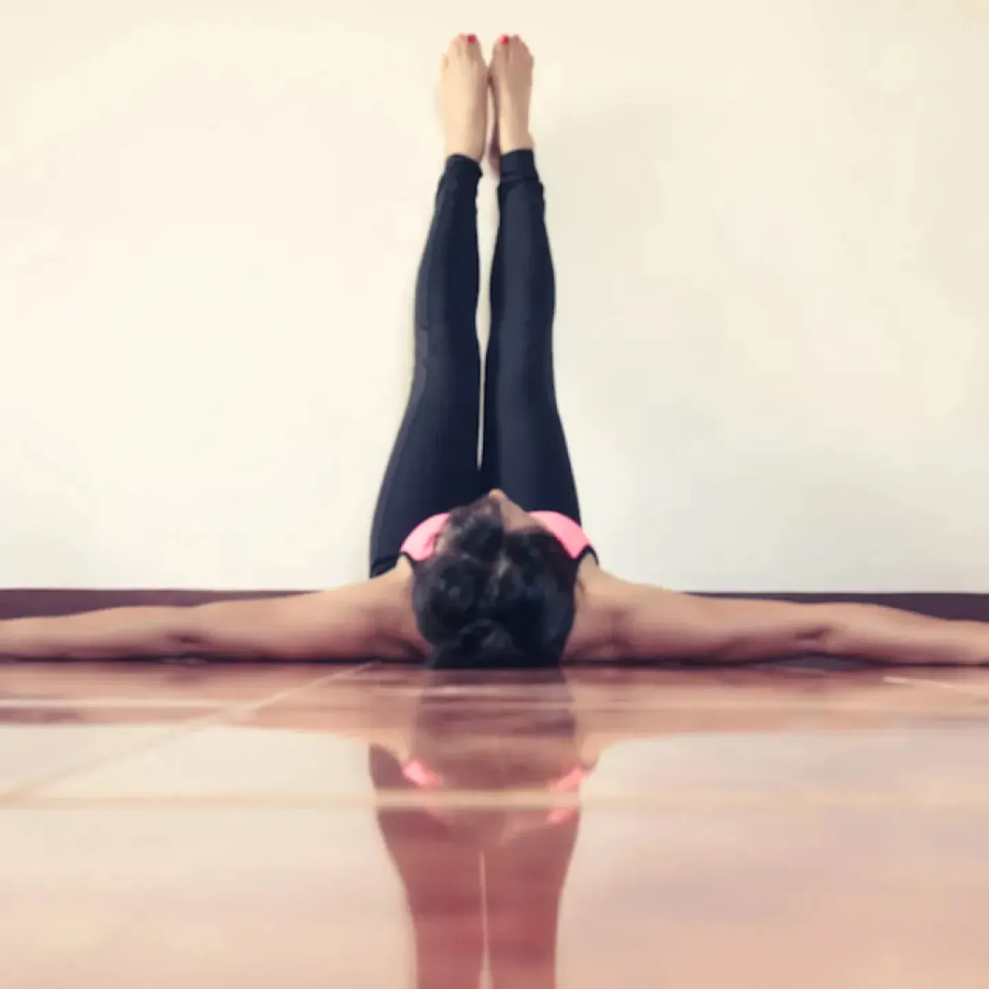 A woman lying on the ground with her legs resting on the wall and her arms spread out to the sides.