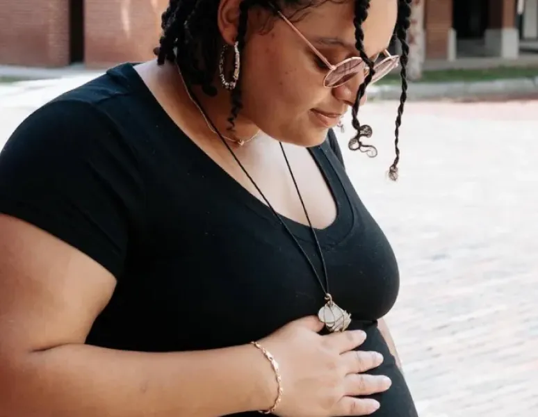 A pregnant individual in sunglasses and a black top looking down at her pregnant belly because she's worried about diastasis rectis abdominis.
