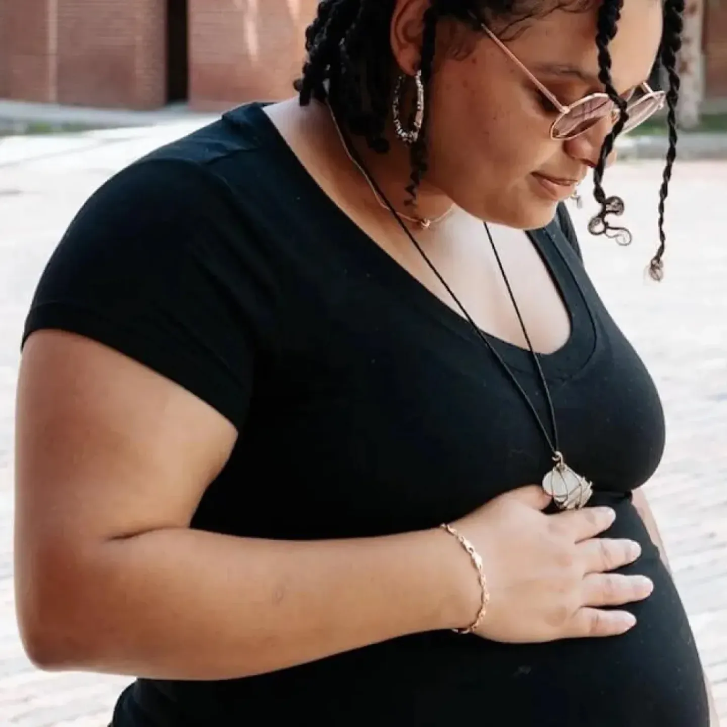 A pregnant individual in sunglasses and a black top looking down at her pregnant belly because she's worried about diastasis rectis abdominis.