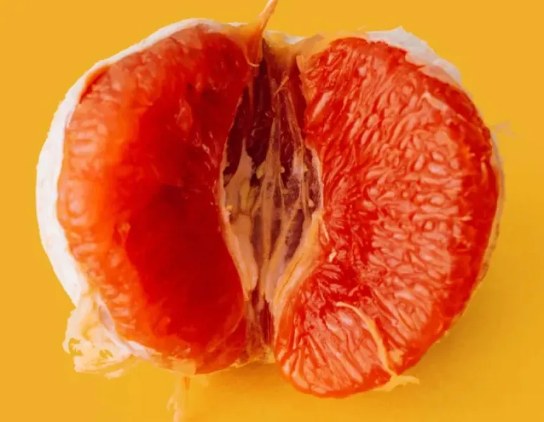 A close-up photo of a peeled, halved blood orange on a mustard yellow background to symbolize high genital esteem and big vulva energy.
