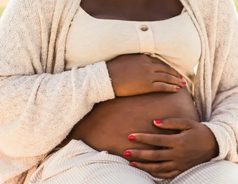 A woman dressed in soft, cream colored clothing, holding her pregnant belly.