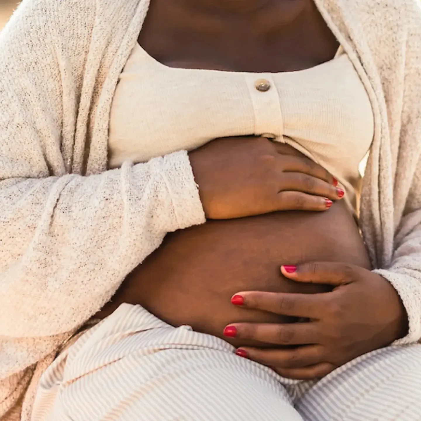 A woman dressed in soft, cream colored clothing, holding her pregnant belly.