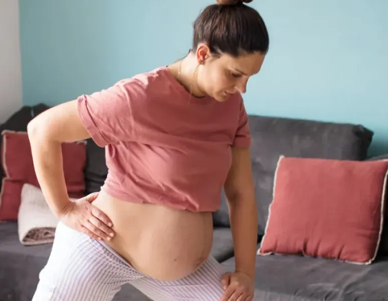 A pregnant person stretches in their living room to help prevent pregnancy pain in their hips, back, and pelvis.