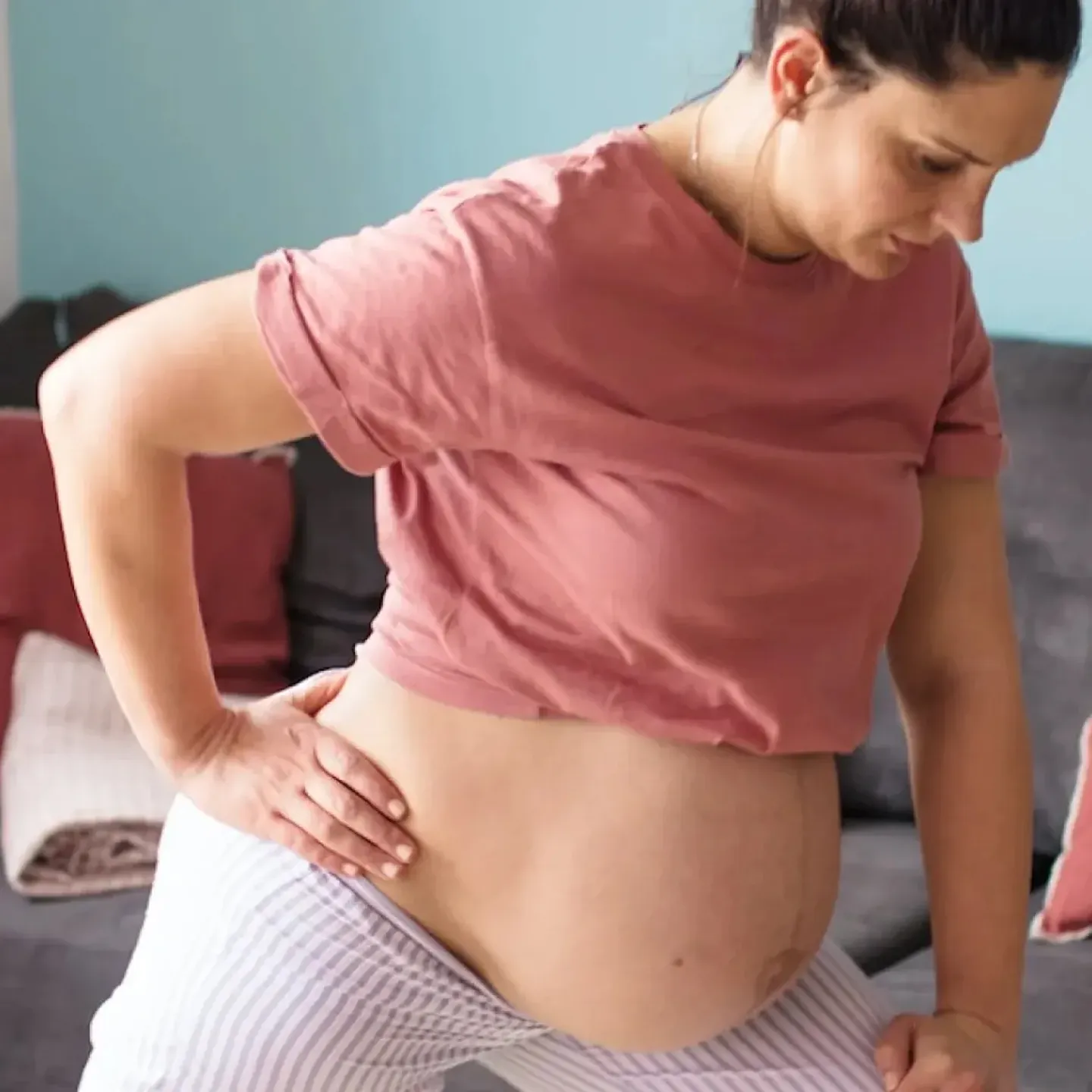 A pregnant person stretches in their living room to help prevent pregnancy pain in their hips, back, and pelvis.
