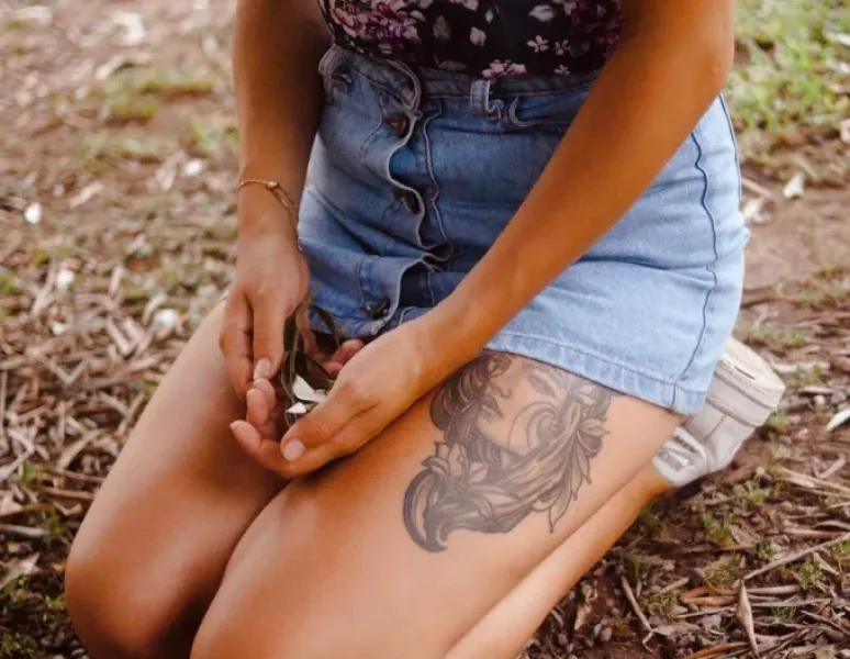 A person sitting down on the ground outside holding a flower in their hands over their bladder.