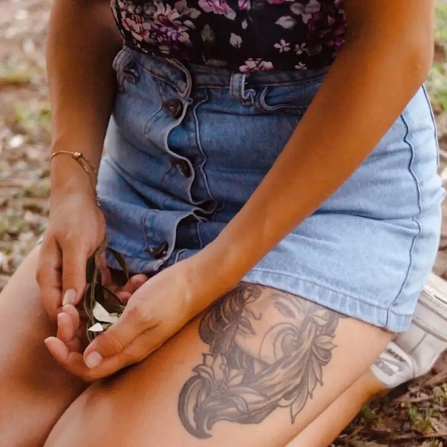 A person sitting down on the ground outside holding a flower in their hands over their bladder.