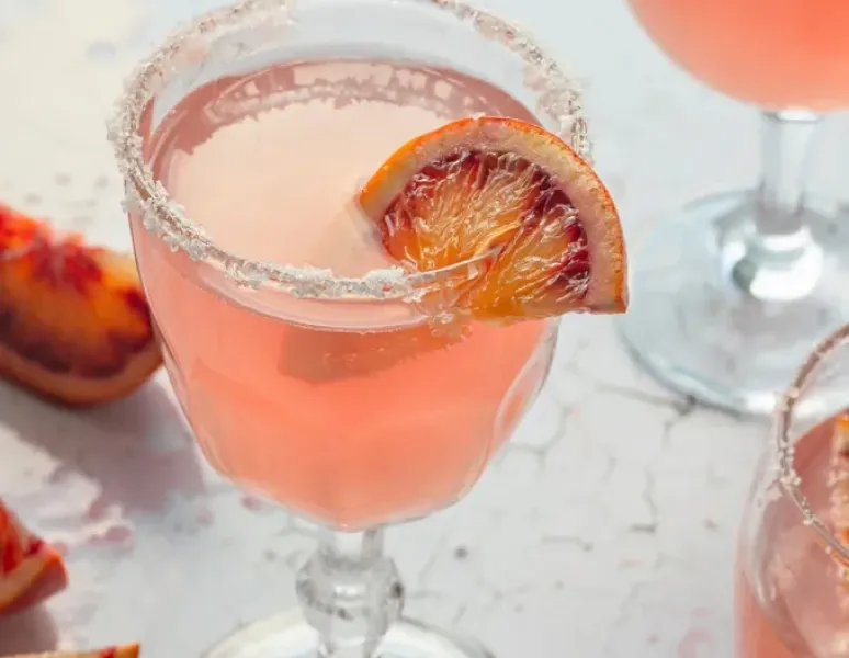 A pink cocktail in crystal stemware with a blood orange garnish and salt rim for a story about bladder irritants.