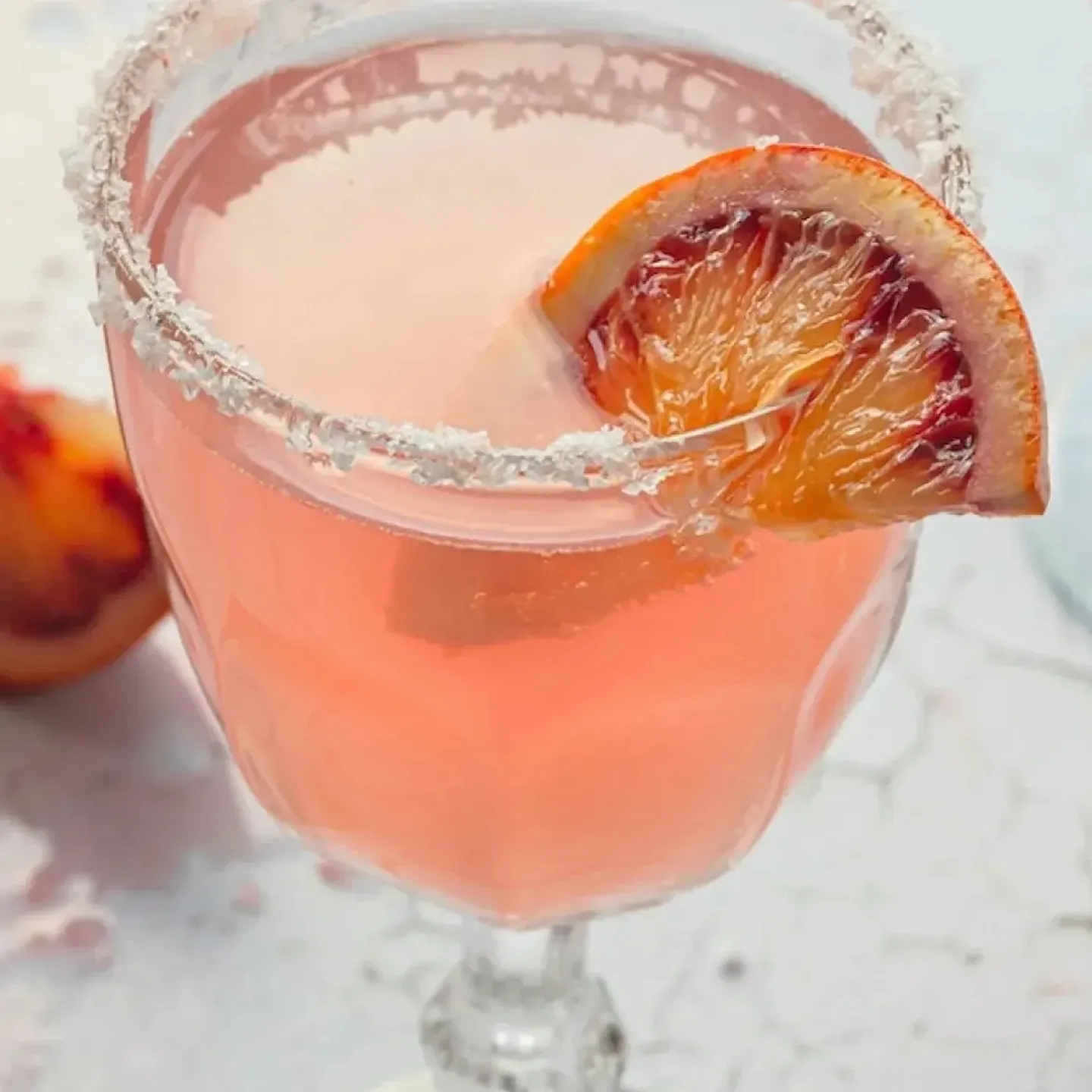 A pink cocktail in crystal stemware with a blood orange garnish and salt rim for a story about bladder irritants.