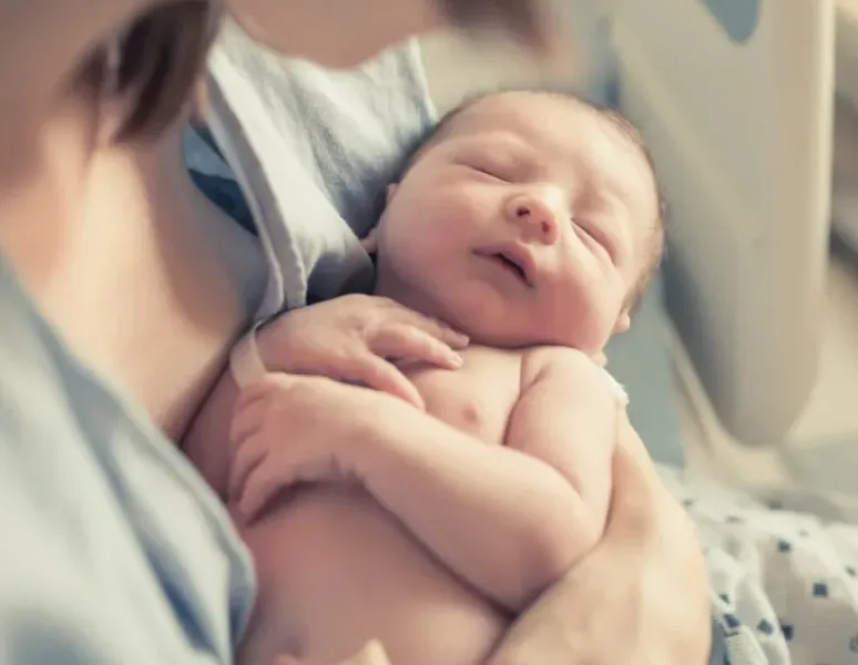 A new mother holding her newborn baby for a story on episiotomy and perineal tear recovery.