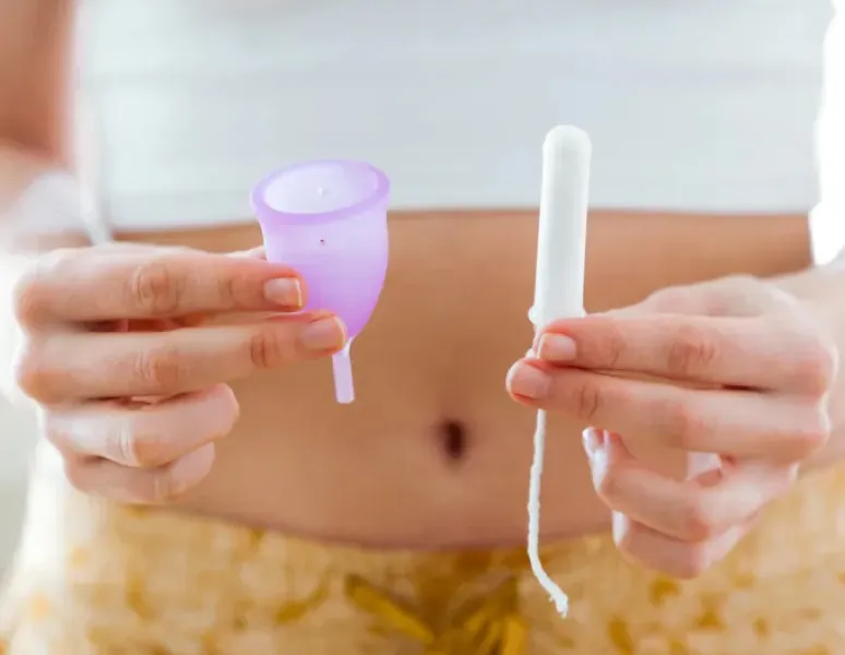 A woman holding up a menstrual cup in one hand and a tampon in the other.