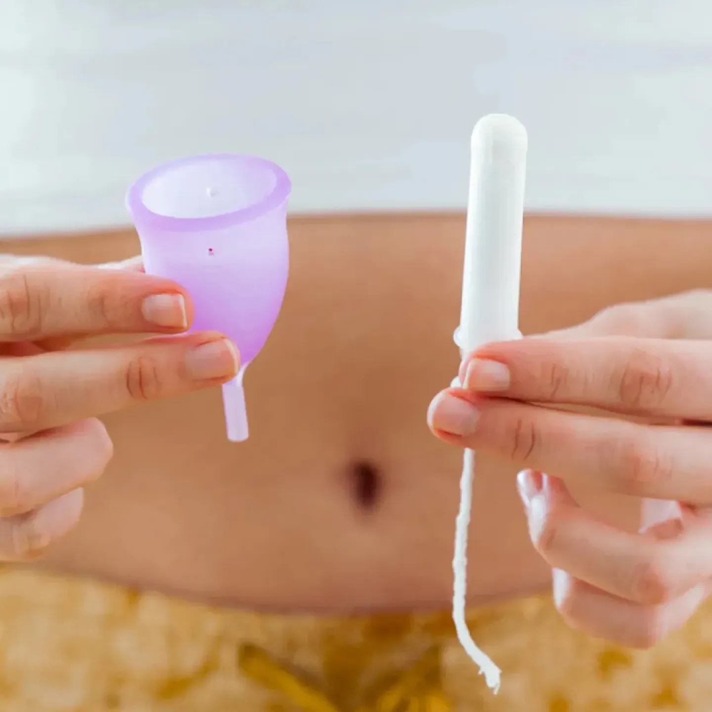 A woman holding up a menstrual cup in one hand and a tampon in the other.