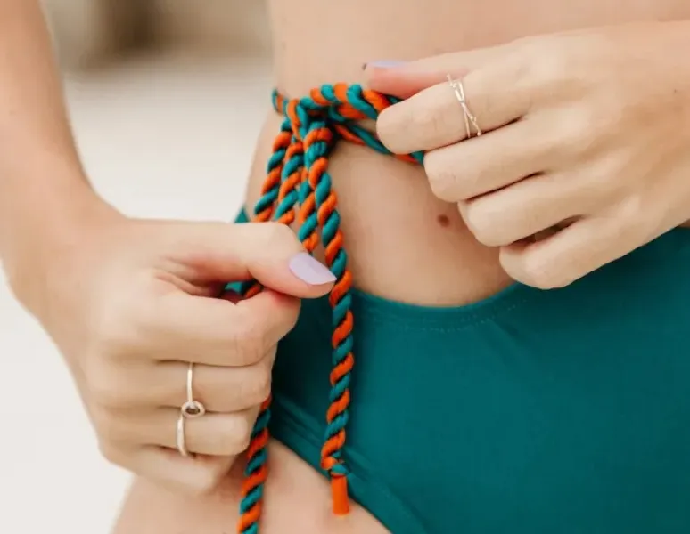 A woman tying a knot in a multi-colored rope that's part of her bikini bottom.