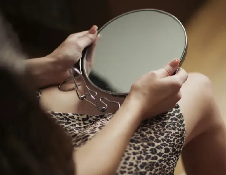 A woman holding a mirror that she's about to use to get a closer look at her clitoris.