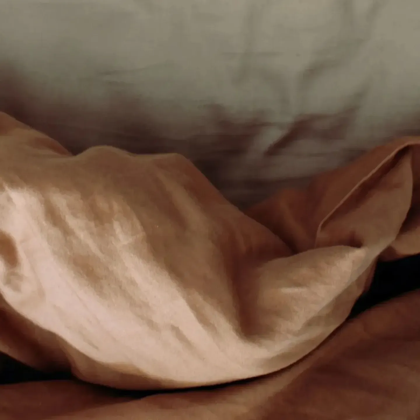 A beige-colored bedspread crumpled up on a bed.