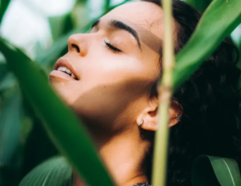 A woman surrounded by lush greenery looking relaxed and self-aware.