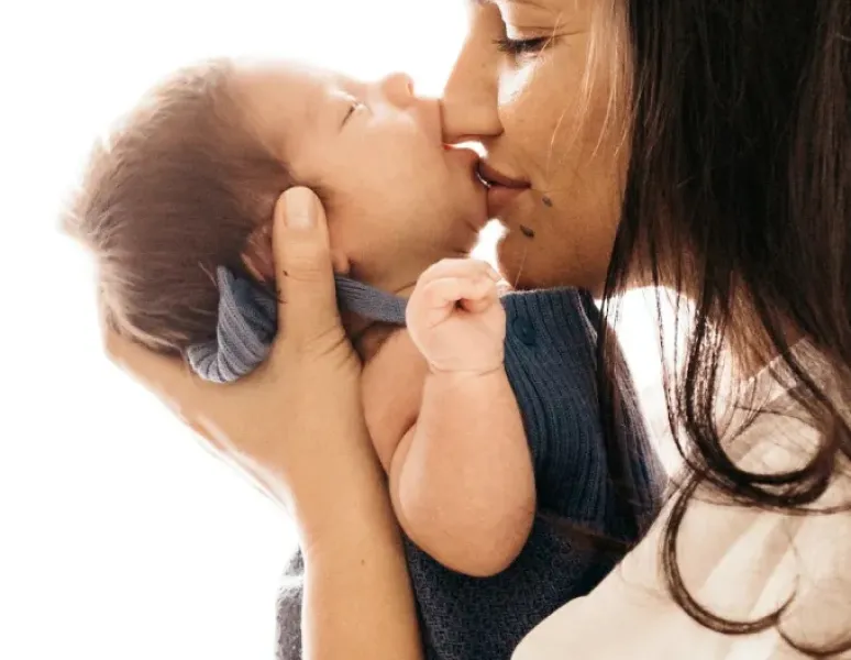 A woman suffering from mommy's wrist supports her baby's head with her hand while baby kisses her on the nose.