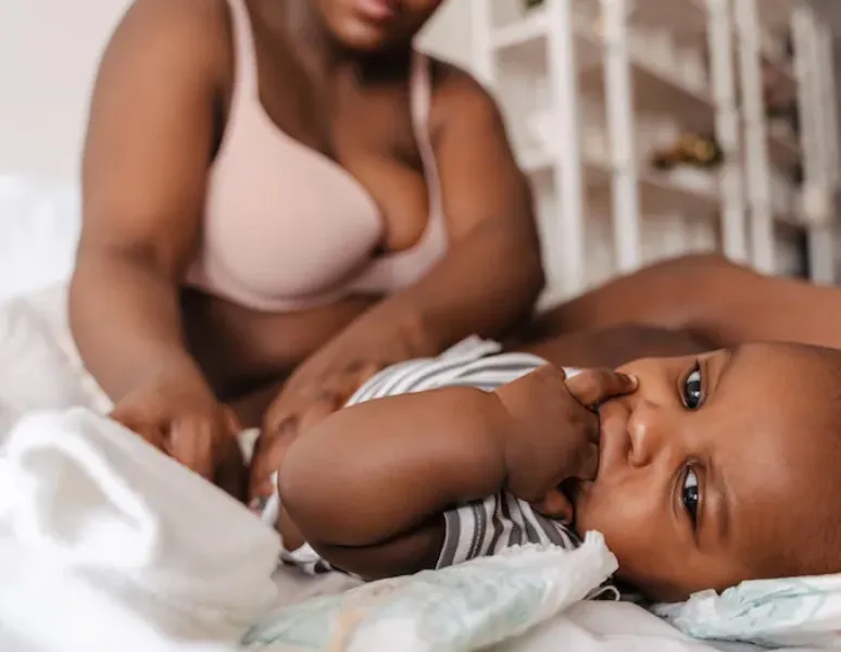 A postpartum mom sitting on her bed, changing her baby's diaper.