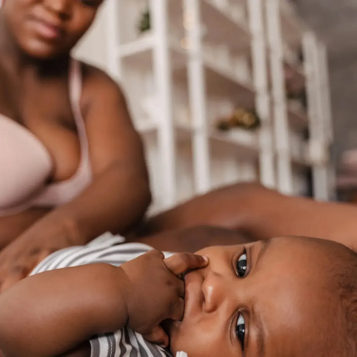 A postpartum mom sitting on her bed, changing her baby's diaper.