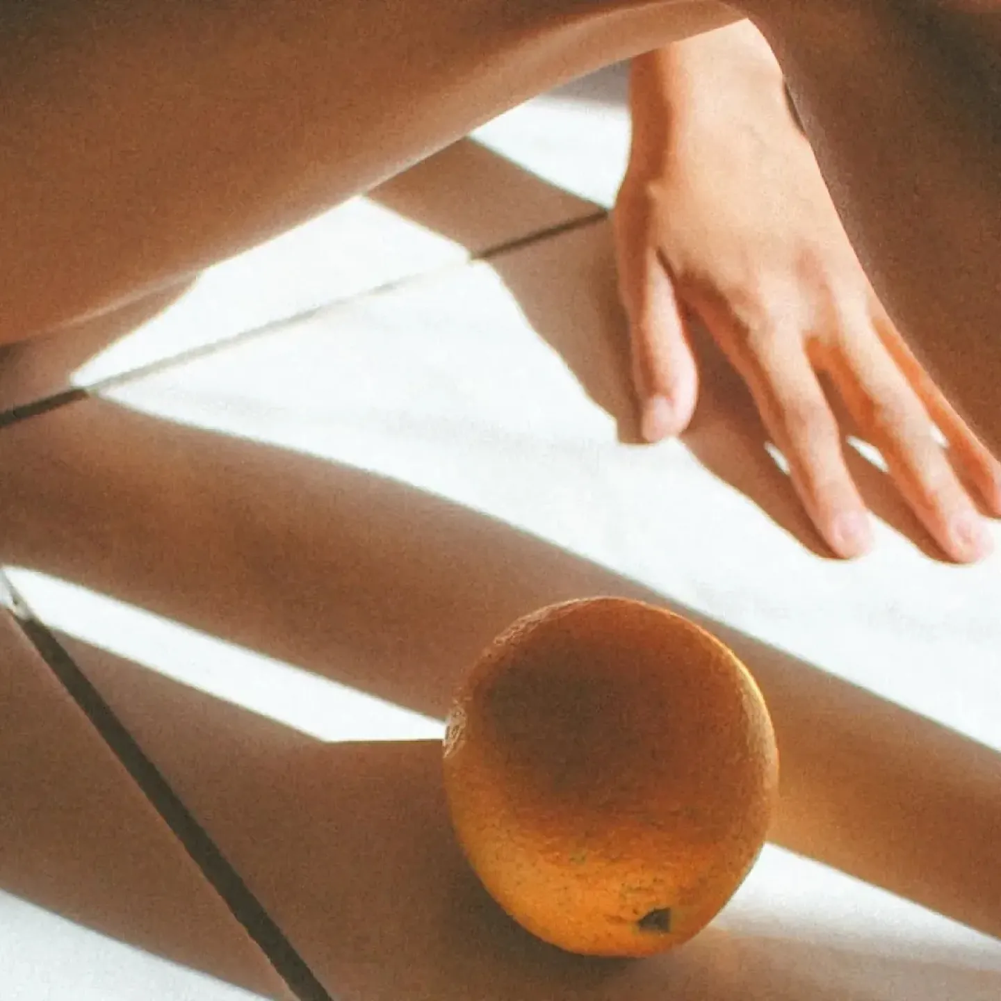 A woman sitting in the sun next to two oranges with artful shadows falling on the floor for story about hysterectomy recovery time.