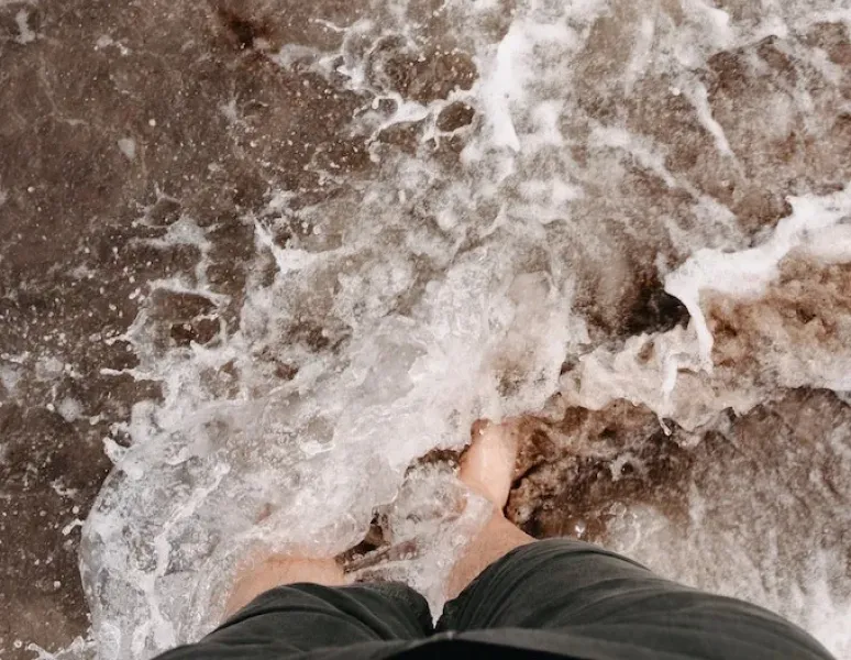 A woman's feet at the edge of the ocean symbolizing the chaotic thoughts that come with postpartum psychosis.
