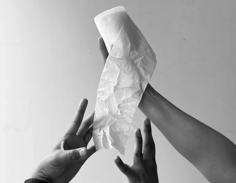 A woman's hand holding out a roll of toilet paper for a story on endless wiping after bowel movements.