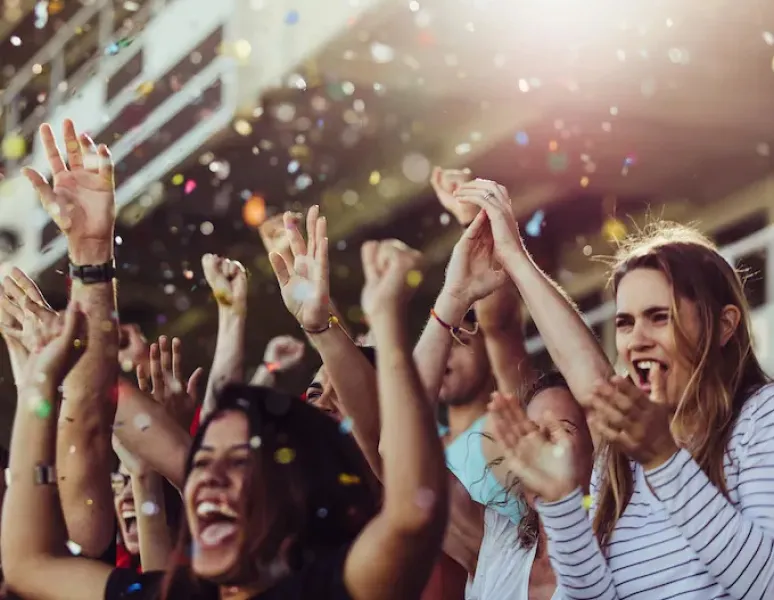 A crowd of women at a stadium cheering with confetti falling from the sky.