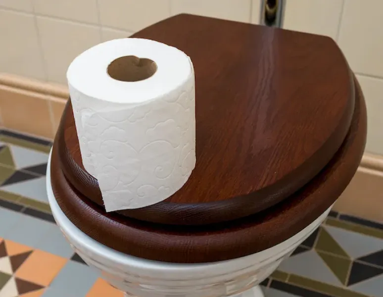 A roll of toilet paper on a wooden toilet seat in a bathroom with colorful tiles.