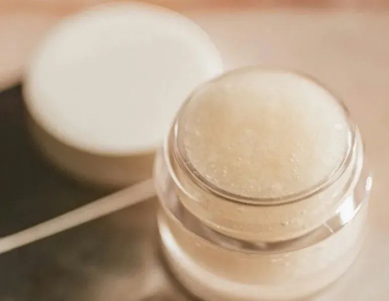 A pot of vulva balm on a marble bathroom counter.