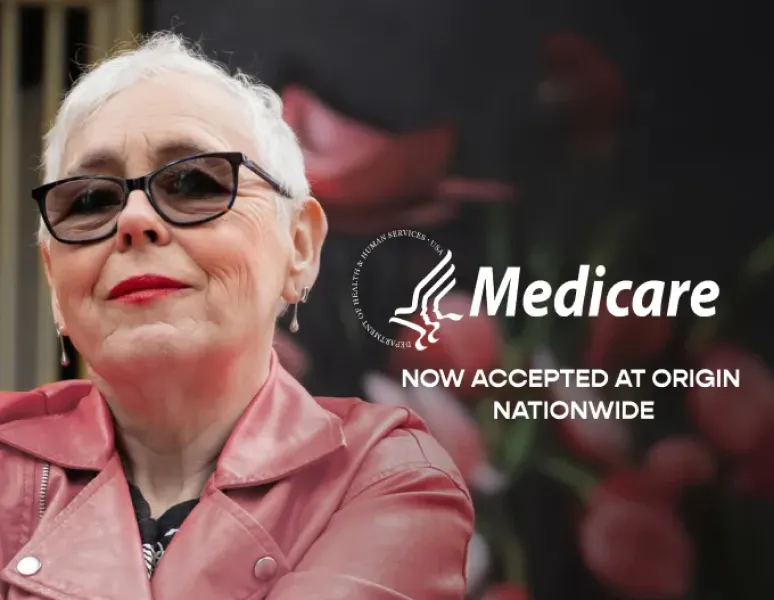 A older woman with close-cropped hair in a leather jacket happy to be able to use Medicare at Origin.