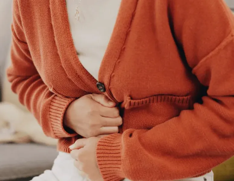 Woman in orange cardigan having crucial abdominal pain.