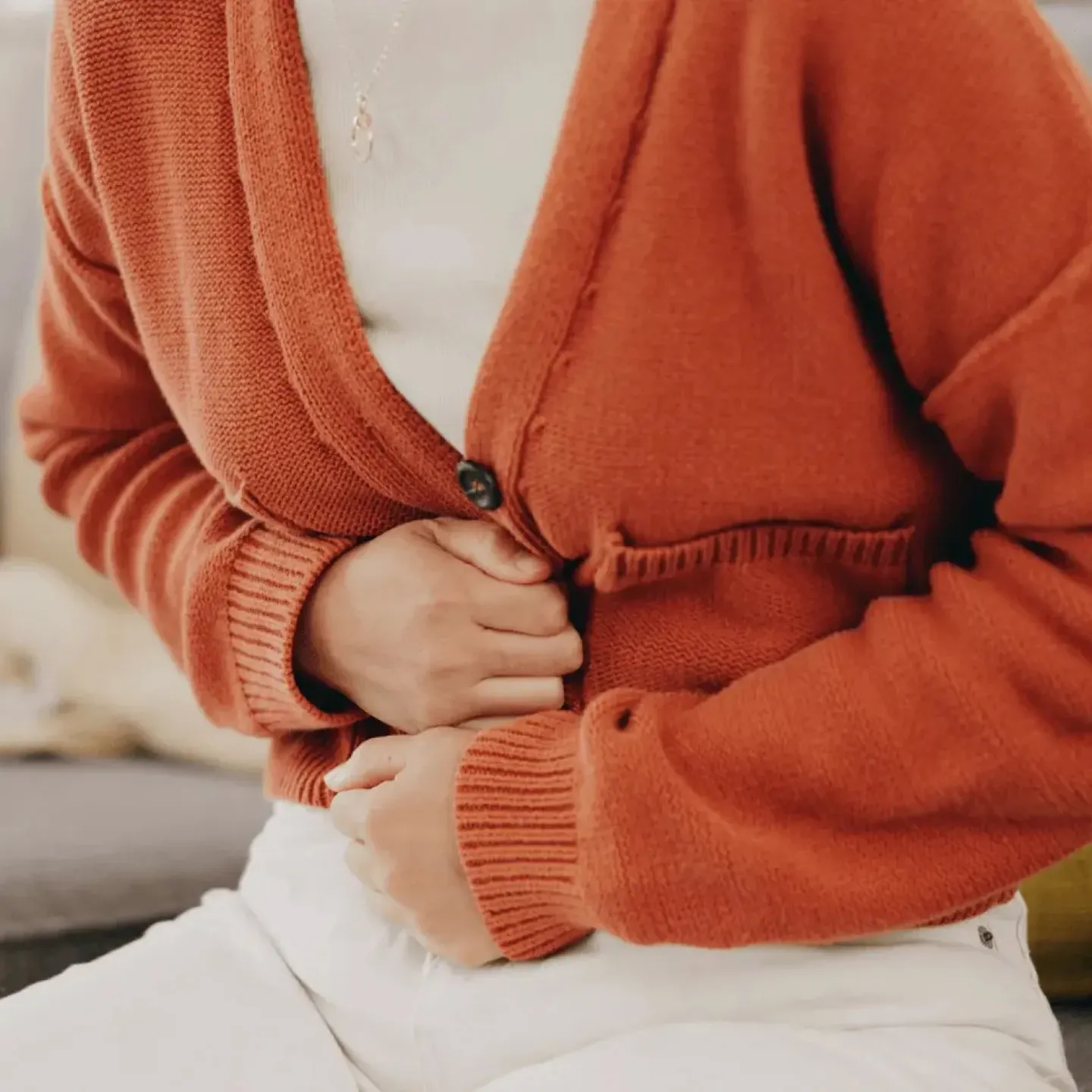 Woman in orange cardigan having crucial abdominal pain.