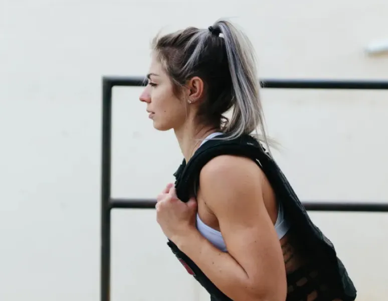 Side profile of a woman doing a squat wearing a weighted vest.
