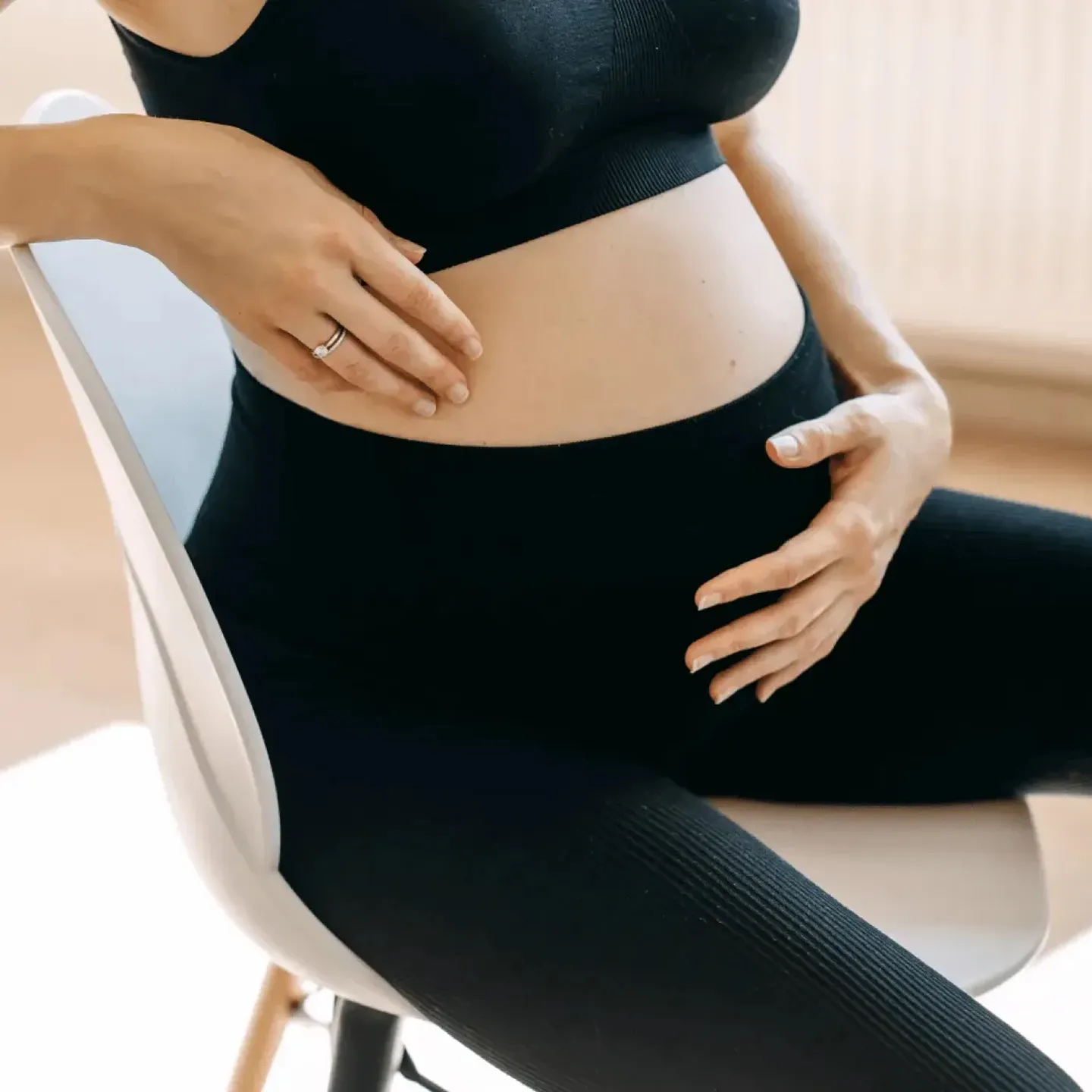 Pregnant woman sitting in a chair holding her stomach representing bladder leaks.