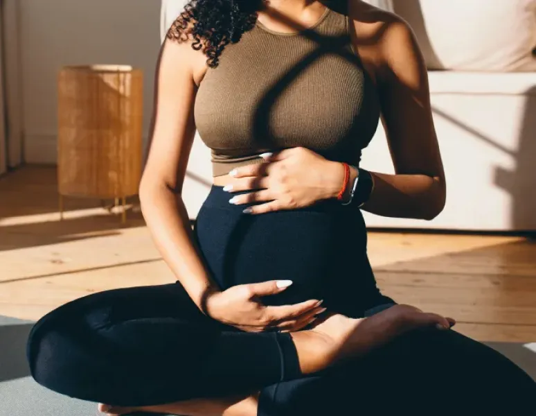 Pregnant woman sitting cross-legged and holding her belly doing breathwork in pregnancy.