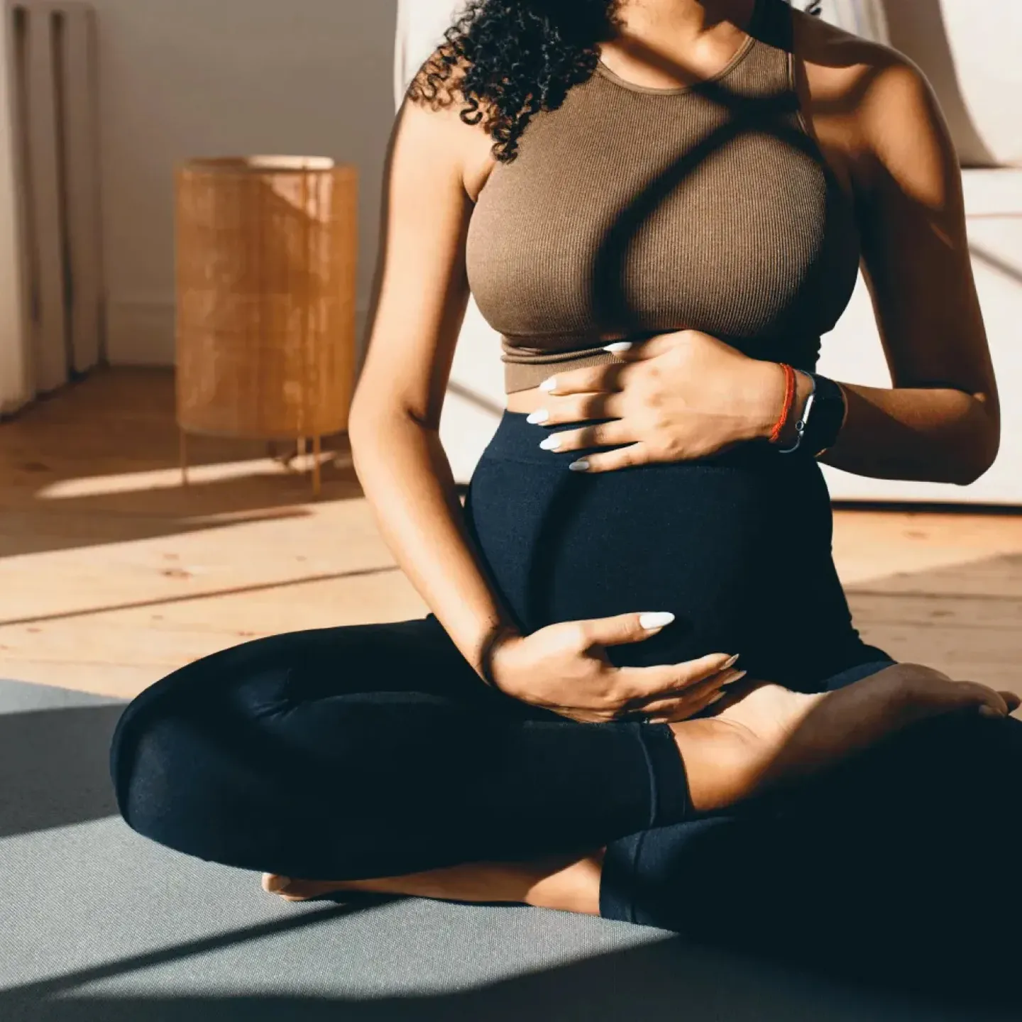 Pregnant woman sitting cross-legged and holding her belly doing breathwork in pregnancy.