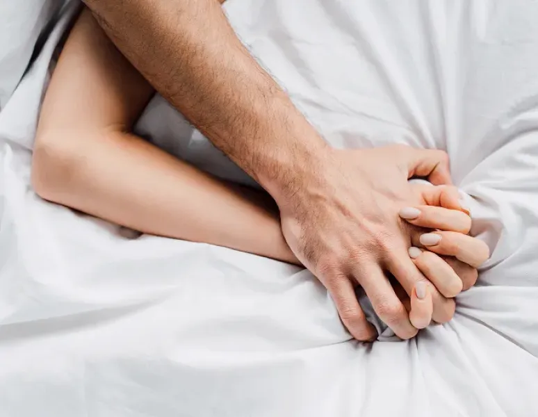 Two people holding hands in bed representing intimacy after cancer treatment.