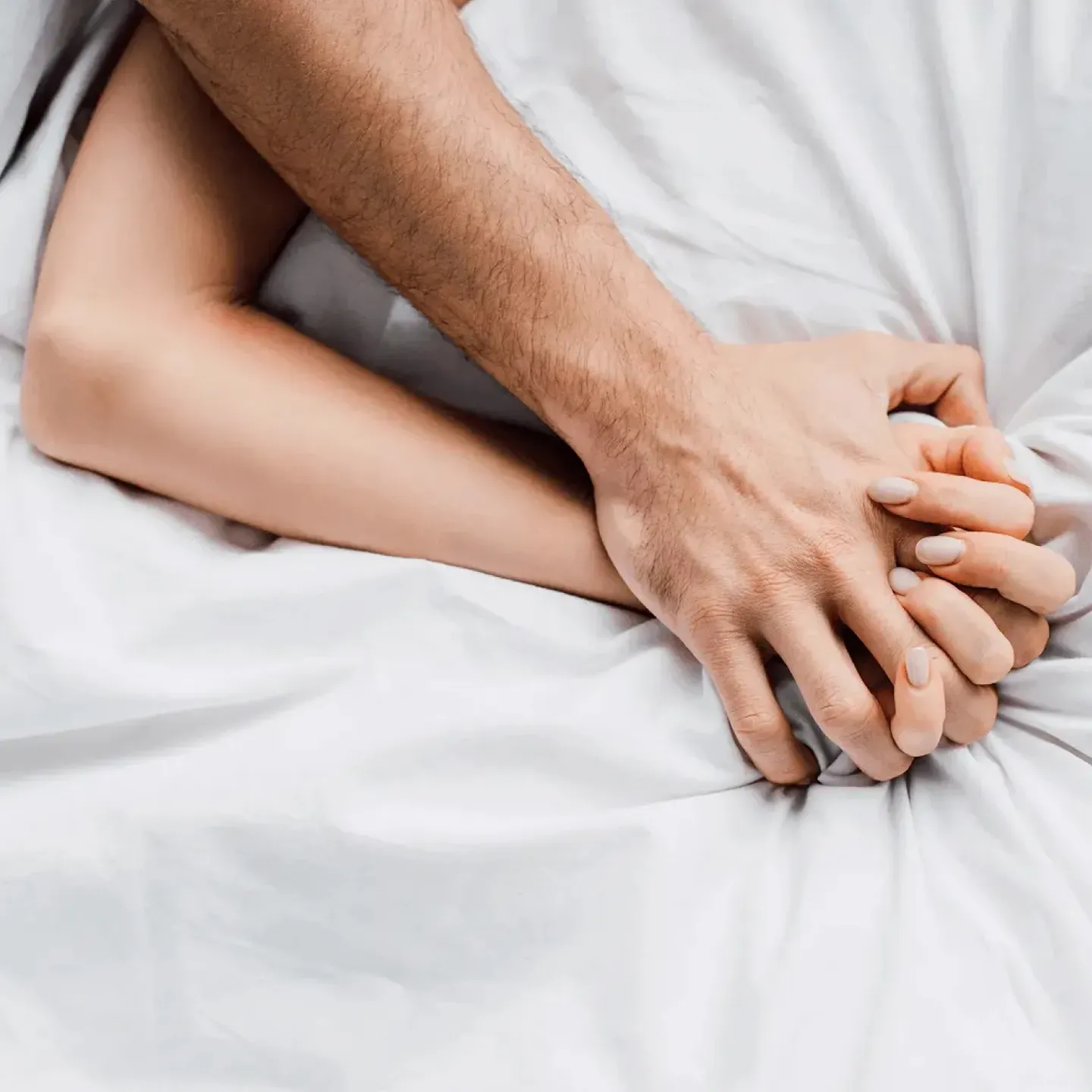 Two people holding hands in bed representing intimacy after cancer treatment.