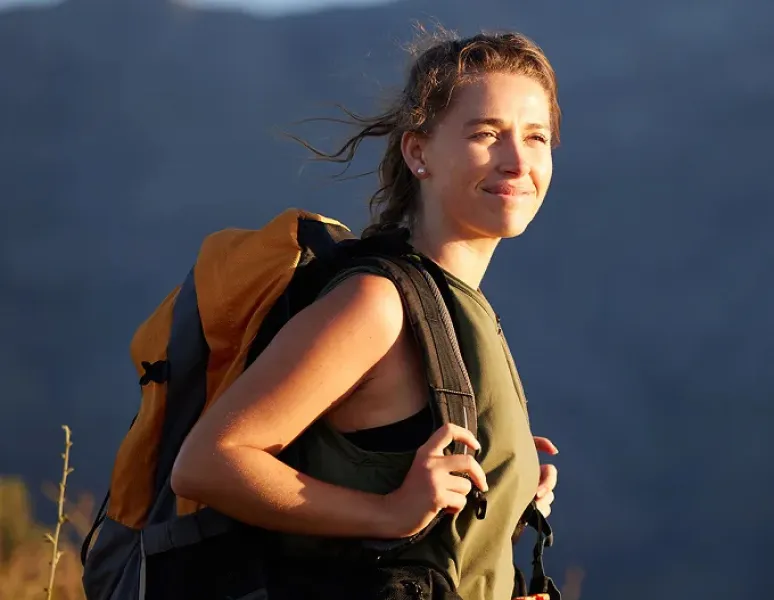 Content woman wearing a backpack outdoors, representing comfort with travel and pelvic health.