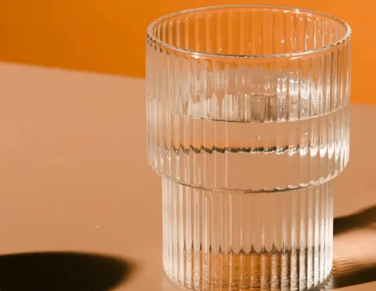 Glass of water on a table with orange background. Represents hydration strategies to avoid back and pelvic pain.