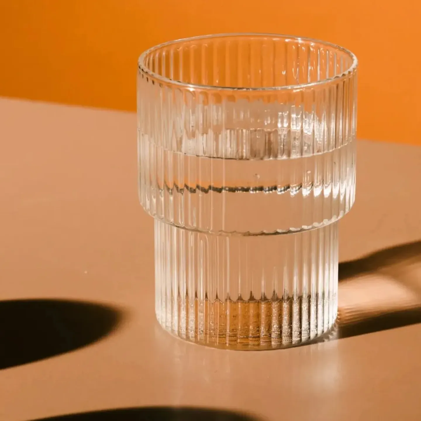 Glass of water on a table with orange background. Represents hydration strategies to avoid back and pelvic pain.