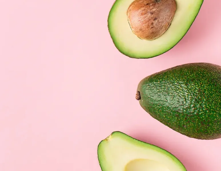 Avocados on a pink backdrop representing Diet to Gain Muscle Mass for women.
