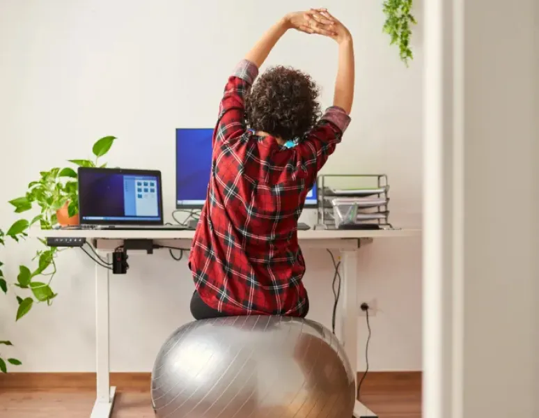 Woman sitting at her ergonomic workstation and doing exercises to support her physical and pelvic health.