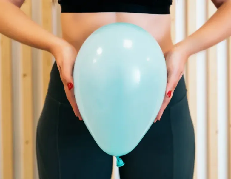 Woman holding inflated balloon in front of her pelvis, representing pelvic floor function what's normal and not normal.
