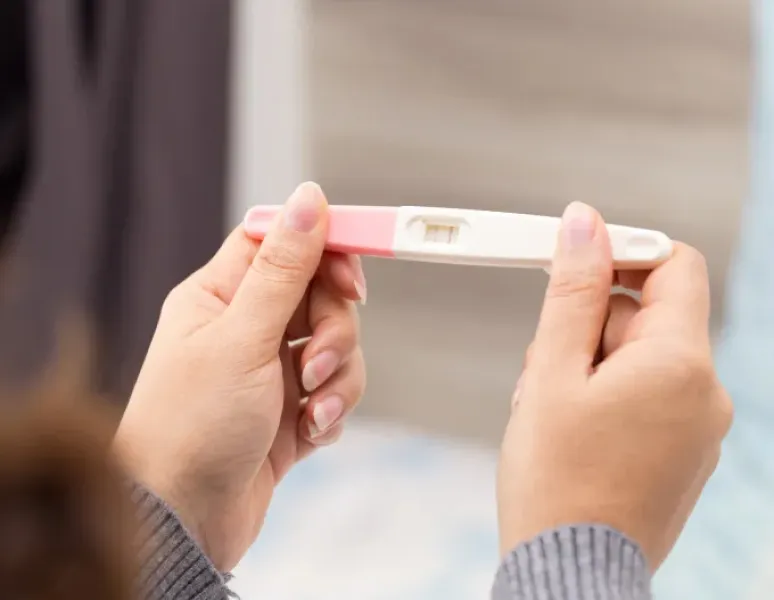 Woman trying to conceive holding pregnancy test representing a guide to preparing to conceive.