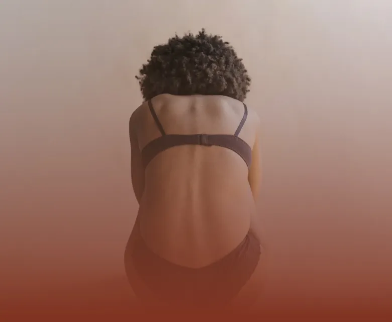 A woman sitting on the floor, bent foward in pain.