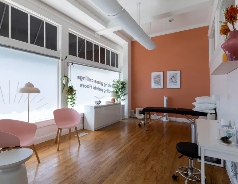 A room in Origin clinic featuring a table, several chairs, and a window allowing natural light to enter.