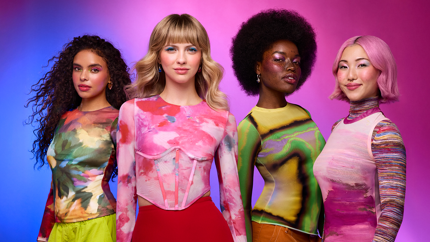 Four diverse women stand confidently side by side in colorful, patterned tops and vibrant backgrounds.
