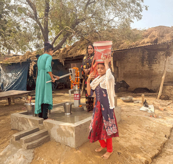 Drei Frauen pumpen frisches Wasser aus einem Brunnen in einem Dorf