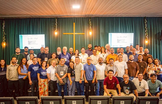 Gruppenfoto von Pastoren und Mitarbeitenden vor einem grünen Vorhang mit Holzkreuz